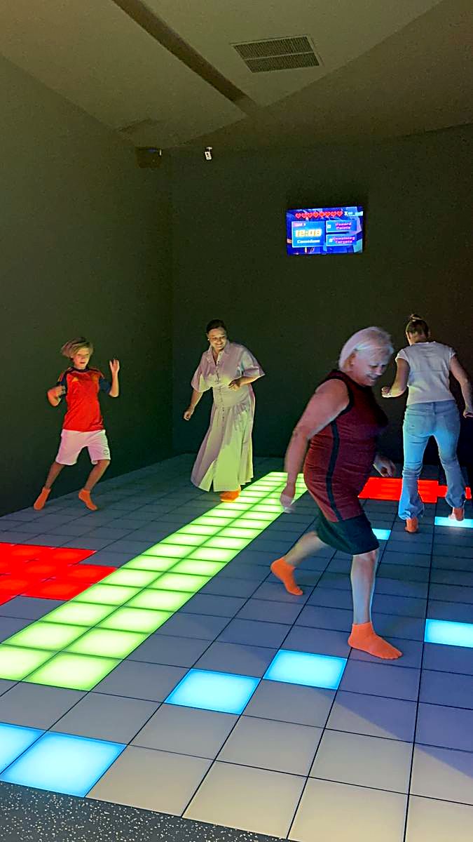Adulți în plină rundă pe podeaua LED Hai Pixel, cu monitorul de scor pe perete