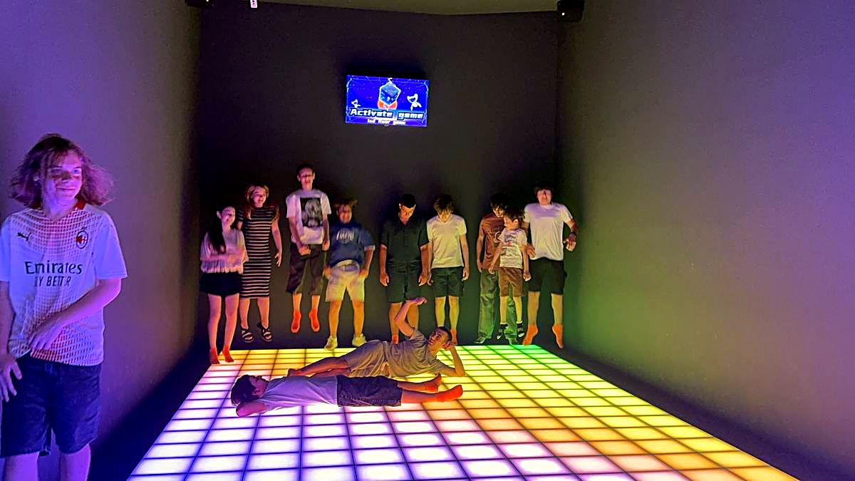 Grup mare de copii jucând pe podeaua LED multicoloră cu ecranul de scor pe perete la Hai Pixel Chișinău