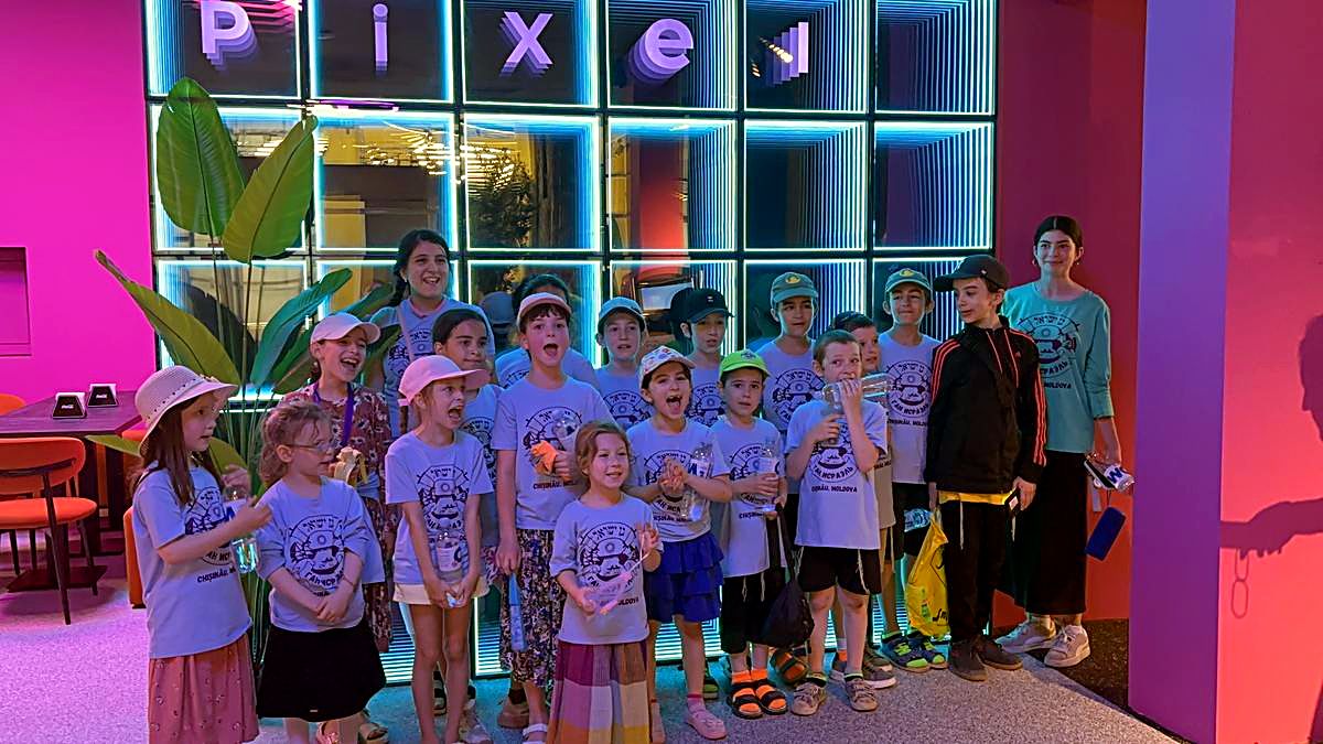 Grup mare de colegi în tricouri identice, aliniați lângă peretele cu litere neon Pixel la Hai Pixel, Chișinău