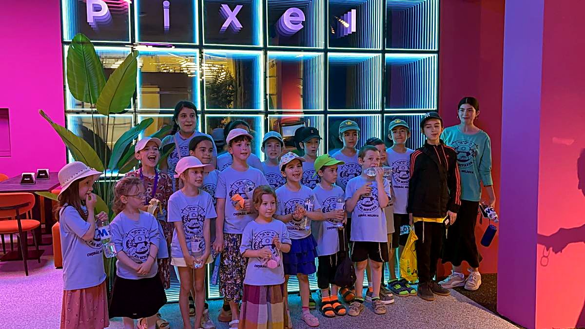Grup mare de copii cu adulții însoțitori pozat în fața peretelui cu litere neon Pixel, Hai Pixel Chișinău
