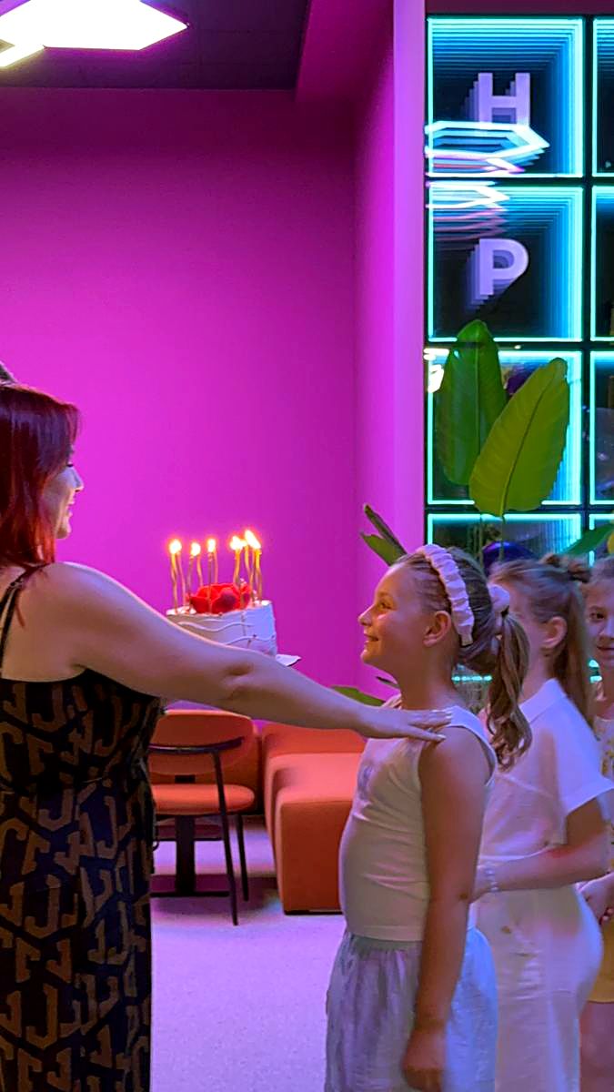 Tort aniversar cu lumânări aprinse dus spre zona de celebrare cu litere neon la Hai Pixel, Chișinău