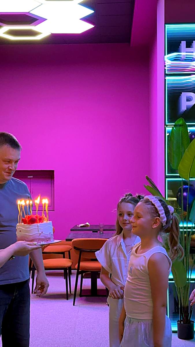 Tortul aniversar adus copilului sărbătorit în zona de celebrare de la Hai Pixel, cu peretele neon în spate