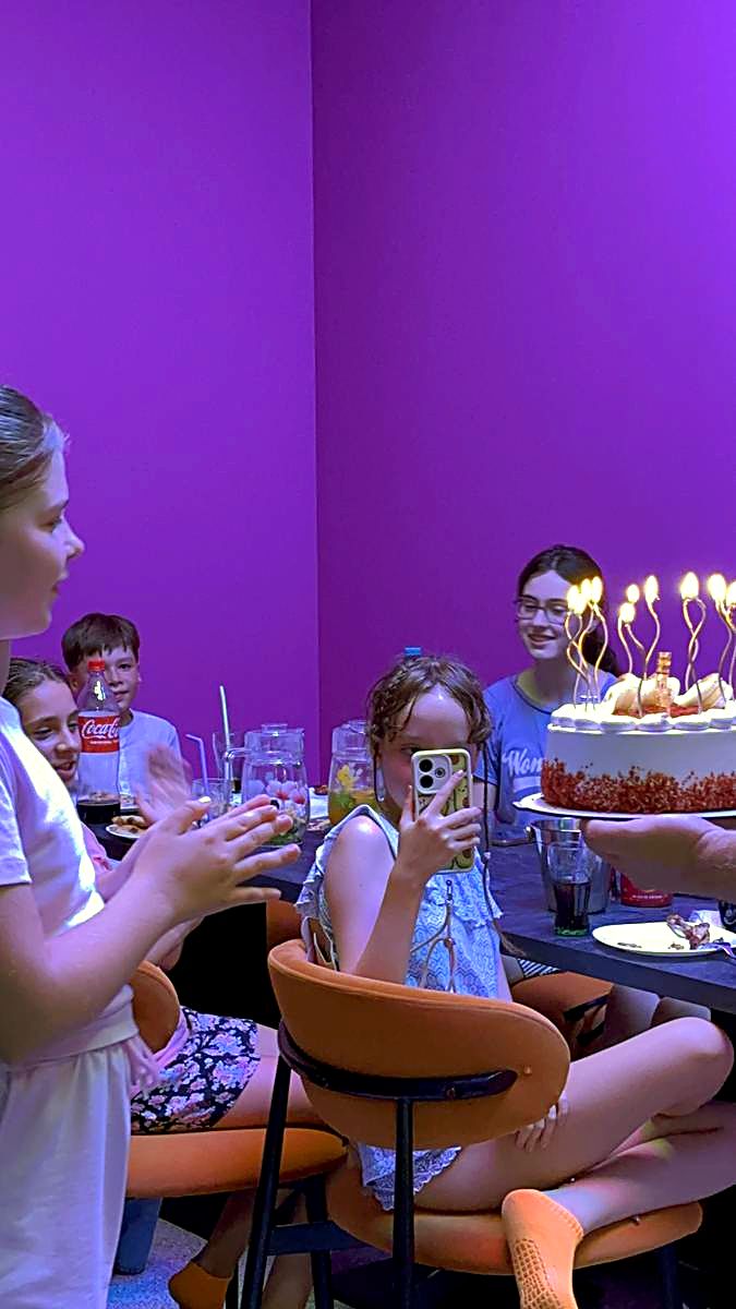Tort aniversar cu lumânări aprinse pe masa din zona de celebrare de la Hai Pixel Chișinău, sub lumini violet